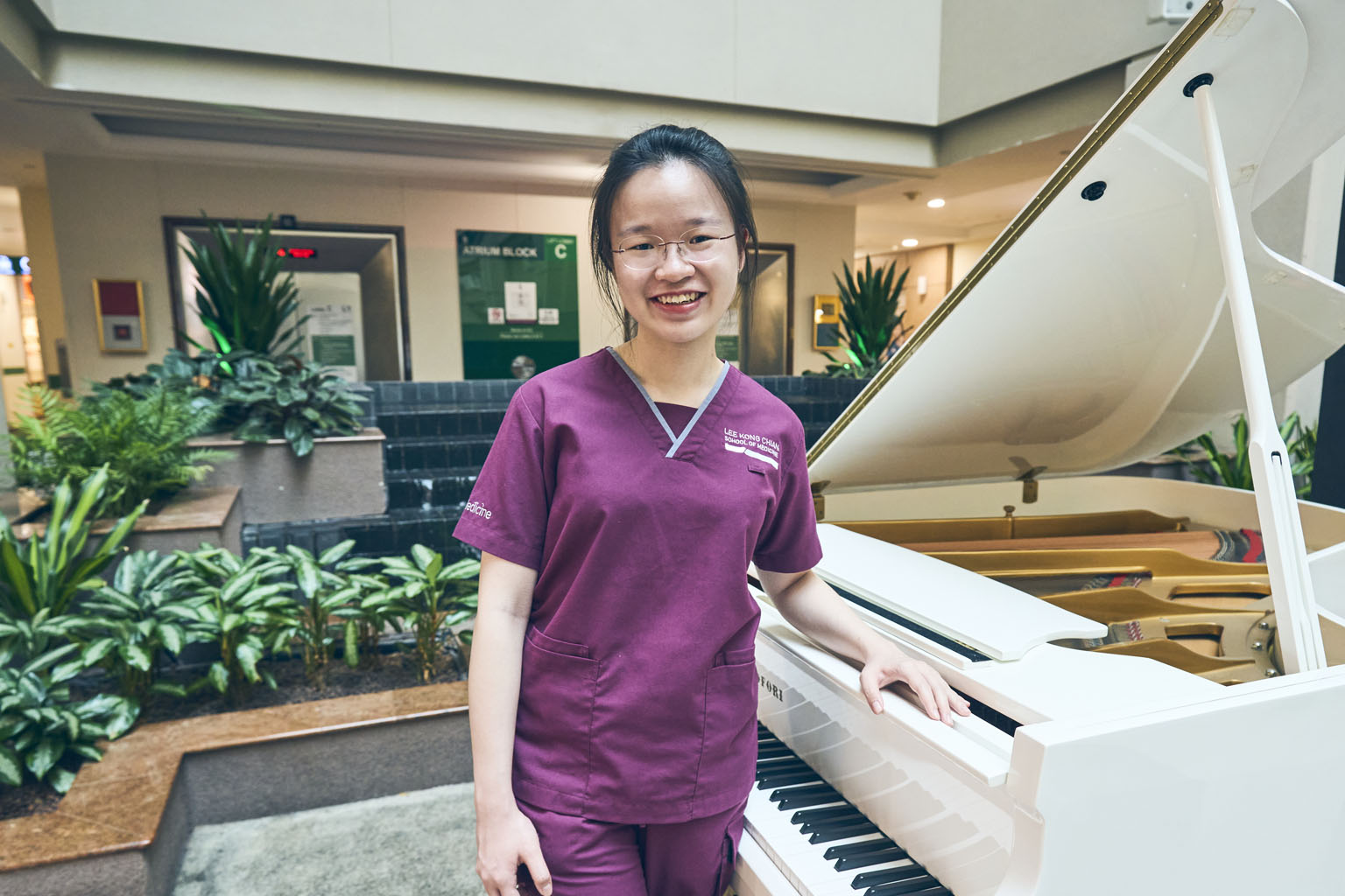 Medical student Loh Pei Yi standing in front of the white grand piano at Tan Tock Seng Hospital