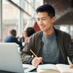Asian university age boy doing research on his laptop